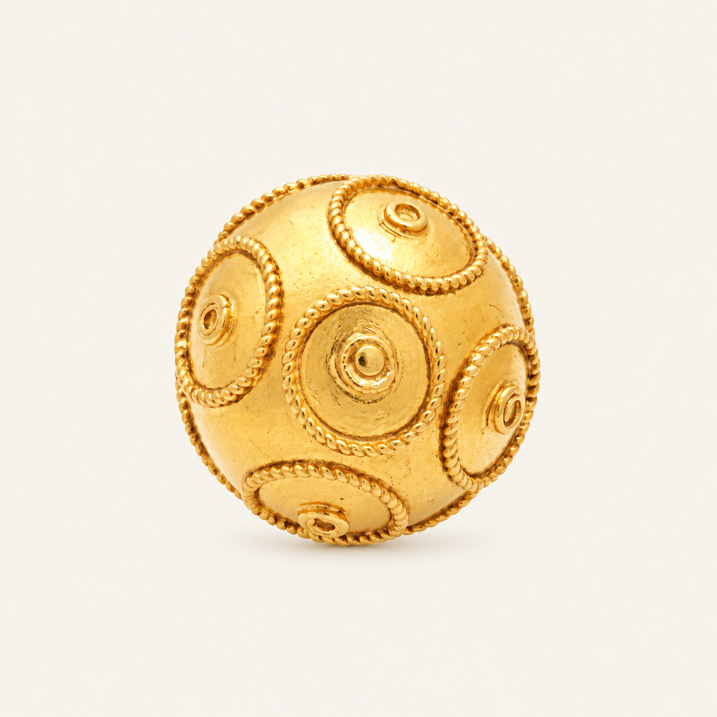 A gold-colored spherical ring with raised circular medallion details and rope-like borders, photographed on a clean off-white background.