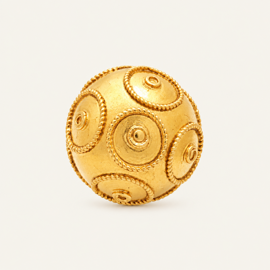 A gold-colored spherical ring with raised circular medallion details and rope-like borders, photographed on a clean off-white background.